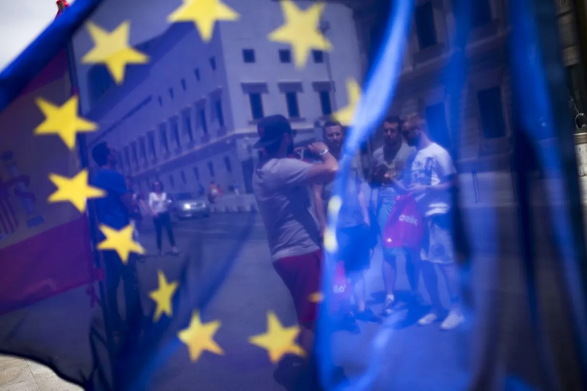 A group of tourists posing for a photograph in front of the Spanish Parliament is seen through the EU flag in Madrid, Spain, on June 24, 2016. (AP Photo/Francisco Seco)