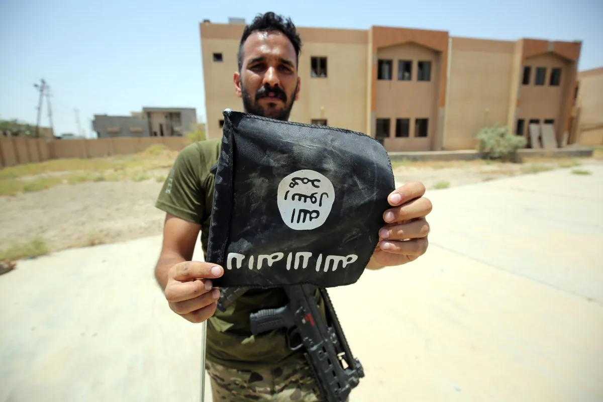 A member of the Iraqi pro-government forces holds an upside down Islamic State (ISIS) flag in a street in Fallujah on June 30, 2016 after recapturing the city from the jihadists. (Ahmad al-Rubaye/AFP/Getty Images)