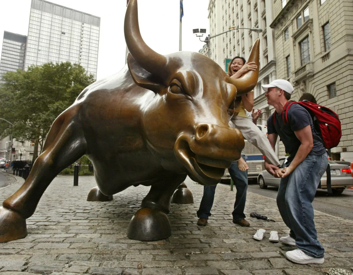 A passerby helps a woman from San Jose, Calif., mount a statue of a bull at the foot of Broadway in the financial district in New York. (Kathy Willens/AP Photo)