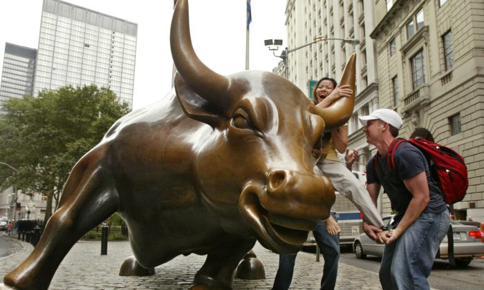 A passerby helps a woman from San Jose, Calif., mount a statue of a bull at the foot of Broadway in the financial district in New York. (Kathy Willens/AP Photo)