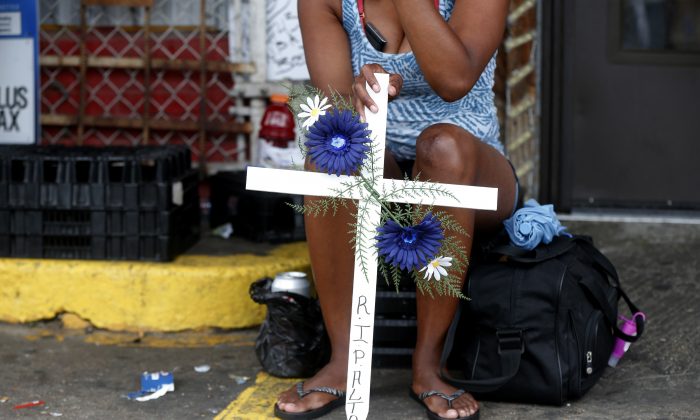Sepia Greene, of Baton Rouge, La., holds a crucifix in memory of Alton Sterling outside the Triple S Food mart in Baton Rouge, La., Monday, July 11, 2016. Sterling was shot and killed last Tuesday by Baton Rouge police while selling CD's outside the convenience store. (AP Photo/Gerald Herbert)