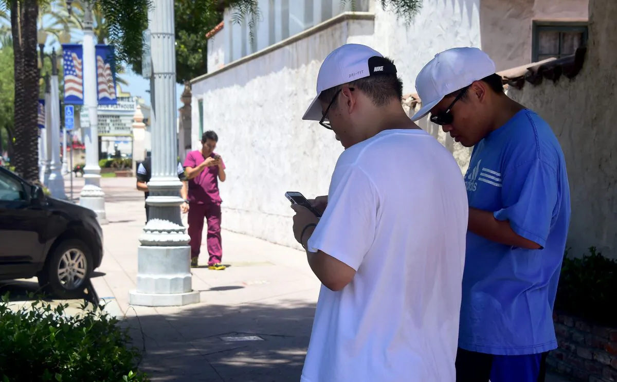 Brothers Jeffrey (L) and Stephen Wang check their cellphones as Tony Luu approaches, all playing Pokemon Go in San Gabriel, Calif., on July 13, 2016. (Frederic J. Brown/AFP/Getty Images)