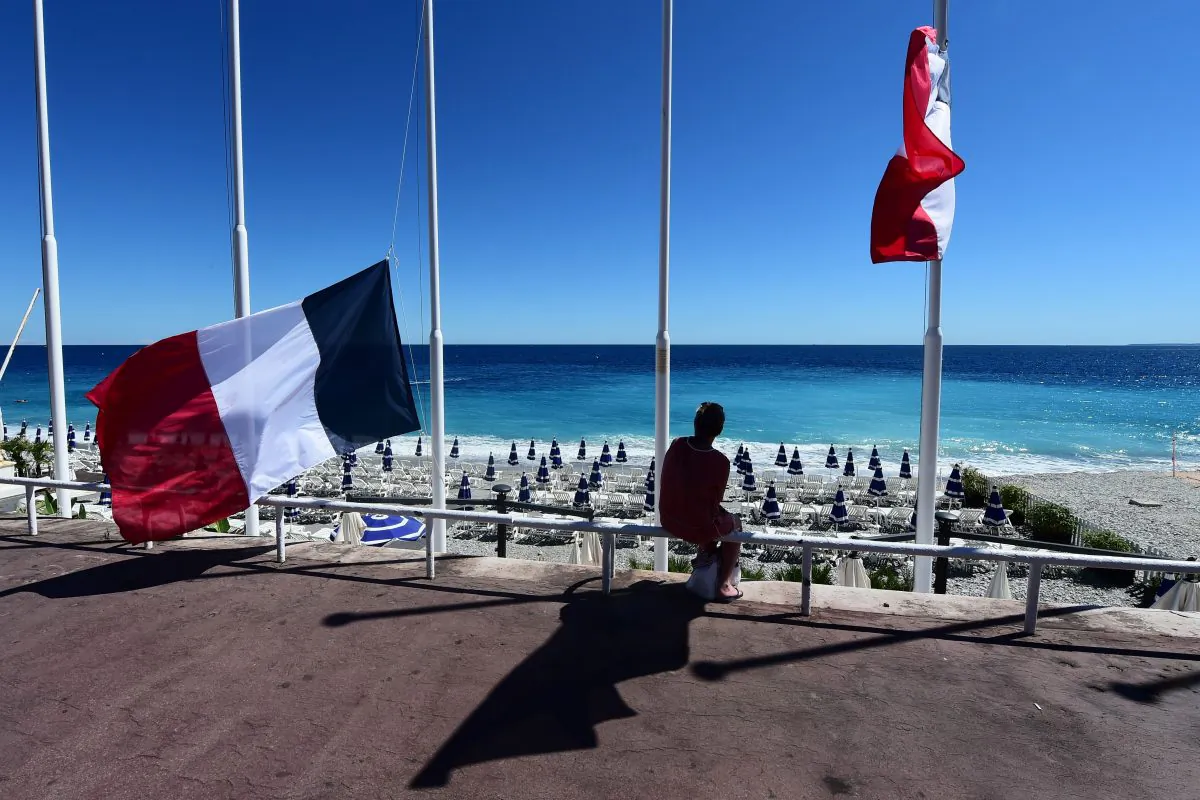 A woman sits under French flags lowered at half-mast in Nice on July 15, 2016, following the deadly Bastille Day attacks.
(GIUSEPPE CACACE/AFP/Getty Images)