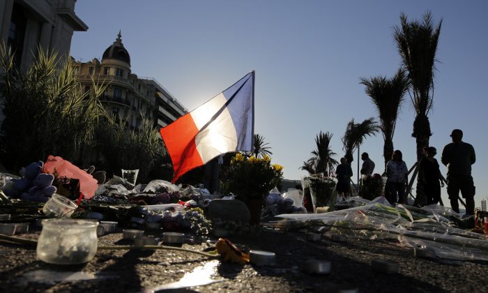 A French flag stands stall amongst a floral tribute for the victims killed during a deadly attack, on the famed Boulevard des Anglais in Nice, southern France, July 17, 2016. (AP Photo/Laurent Cipriani)