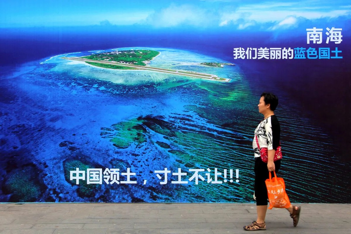 A woman walks past a billboard featuring an image of an island in South China Sea on display with Chinese words that read: "South China Sea, our beautiful national territory, we won't let go an inch," in Weifang, east Shandong Province, China, on July 14, 2016. (Chinatopix via AP)
