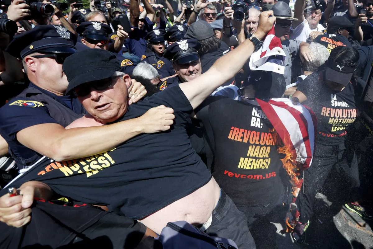 A law enforcement officer clashs with protester who is holding a burning  American flag, Wednesday, July 20, 2016, in Cleveland, during the third day of the Republican convention. (AP Photo/John Minchillo)