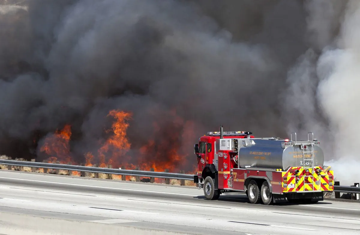 A Los Angeles County Fire water tender fire truck sprays down flames as they near the northbound Highway 14 during the Sand Fire in Santa Clarita on July 22, 2016. (Katharine Lotze/The Santa Clarita Valley Signal via AP)