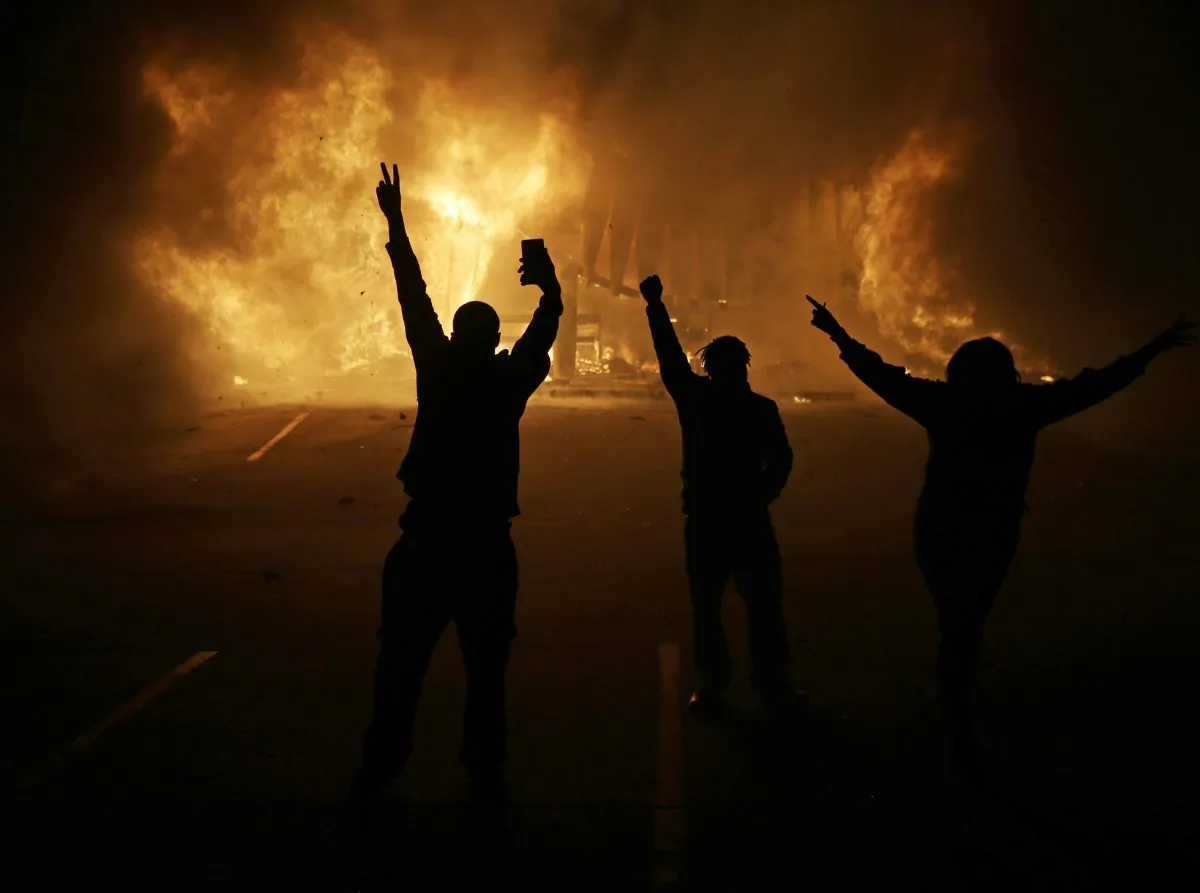 People watch as stores burn in Ferguson, Mo., on Nov. 25, 2014. (AP Photo/David Goldman)