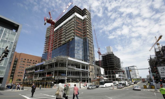 In this Thursday, May 19, 2016, photo, passers-by walk near the construction site a high-rise building in Boston. On Friday, July 29, 2016, the Commerce Department issues the first estimate of how the U.S. economy performed in the April-June quarter. (AP Photo/Steven Senne)