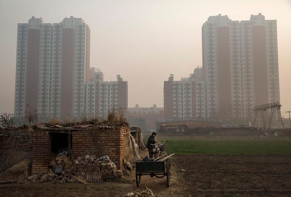 An elderly Chinese farmer stands outside her home on farmland backdropped by a new housing development in Hebei on Nov. 21, 2014. (Kevin Frayer/Getty Images)