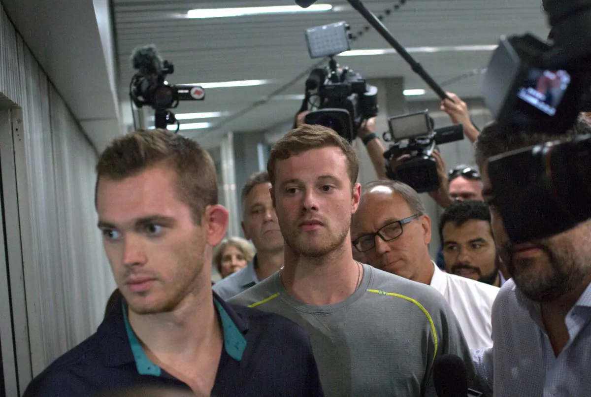 Journalists surround American Olympic swimmers Gunnar Bentz, left, and Jack Conger, center, as they leave the police station at Rio International airport Aug. 18, 2016. (AP Photo/Mauro Pimentel)