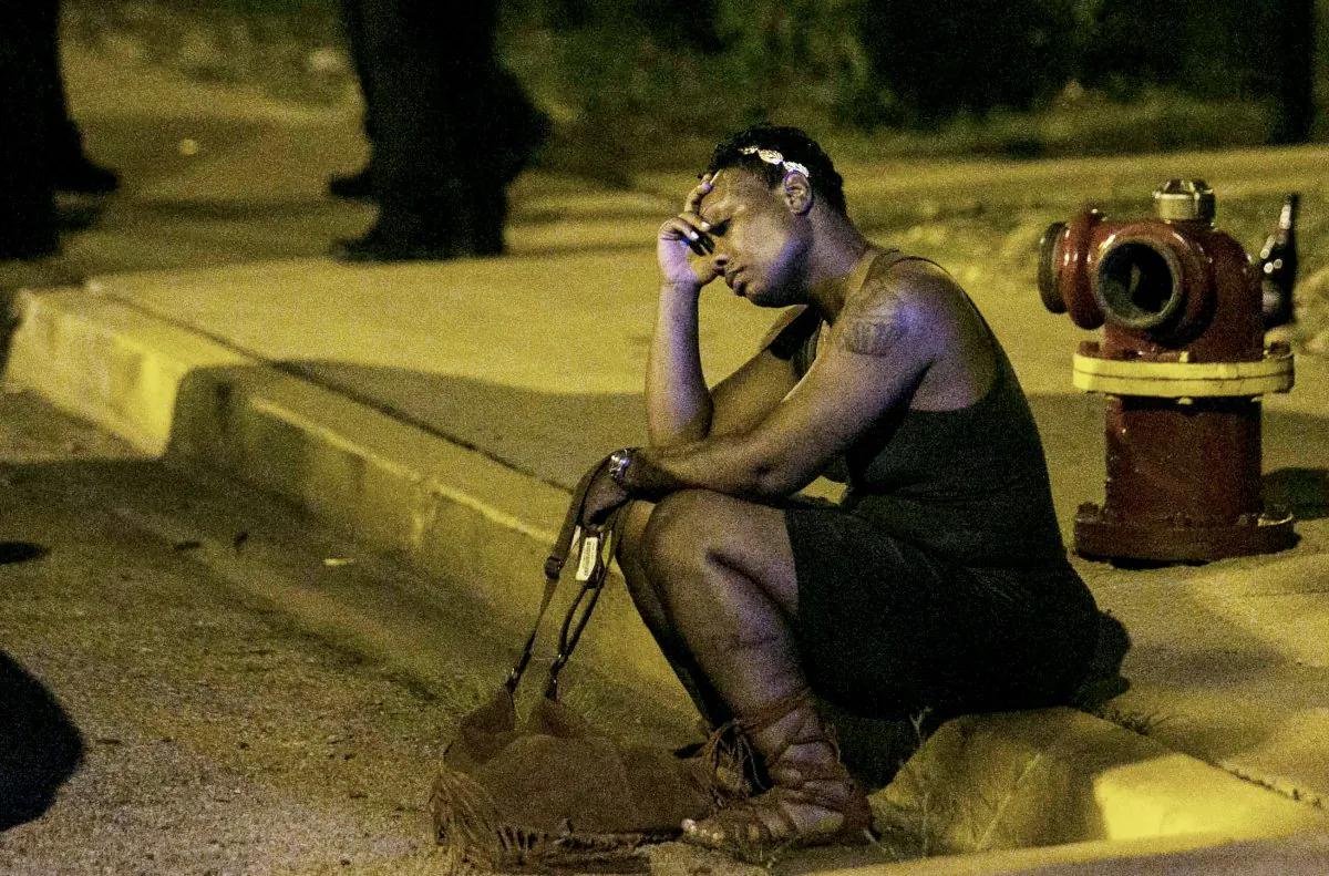 In this Aug. 7, 2016, photo, a woman sits on the curb as police in the background investigate the scene where gunfire at a birthday party left a man dead and a woman injured.  (Ashlee Rezin /Chicago Sun-Times via AP)