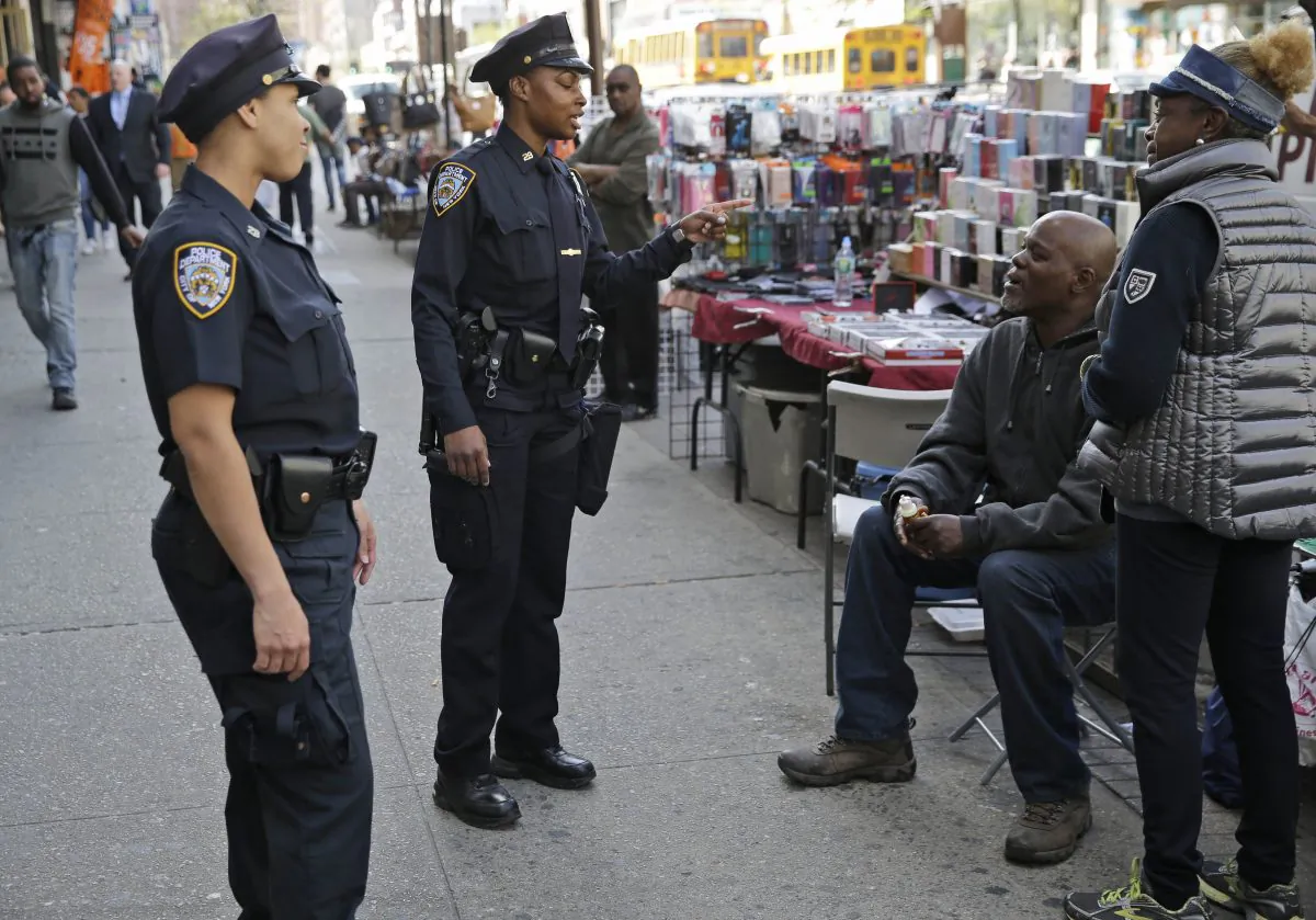 Police officers Lanora Moore, left, and Shakara President talk with a vendor on 125th Street in the Harlem section of New York, Wednesday, April 29, 2015. (AP Photo/Seth Wenig)