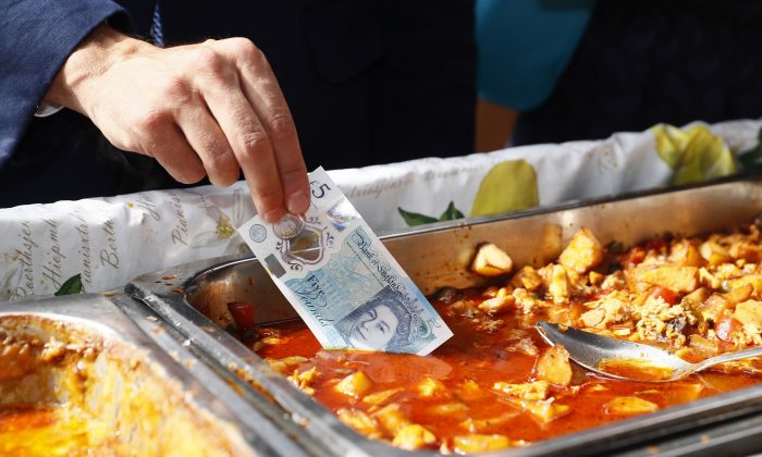 Bank of England Governor Mark Carney dips a new plastic £5 note into a tray of food as he buys lunch from a stall at Whitecross Street market in London, Tuesday, Sept. 13, 2016. The polymer fiver is said by the Bank of England to be cleaner, safer and stronger than paper notes, lasting around five years longer. (Stefan Wermuth/Pool Photo via AP)