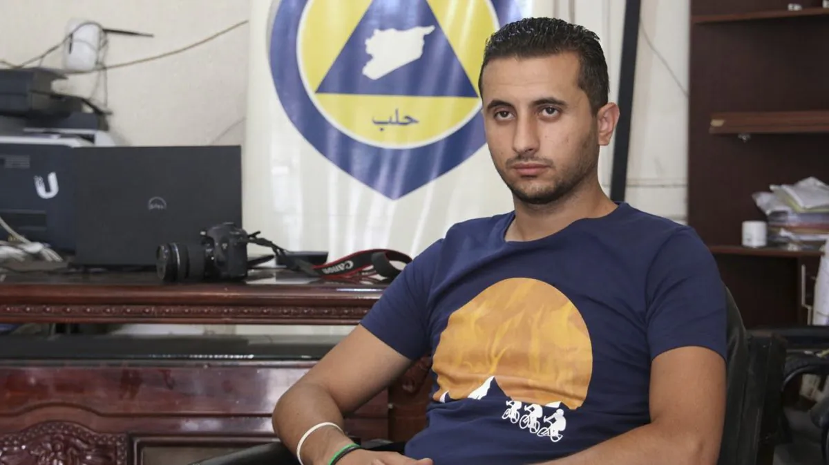Ibrahim Alhaj, 26-year old member of Syrian Civil Defense, also known as White Helmets, sits in front of a banner for the first responders rescue group in Aleppo, Syria, in August 2016. (Handout from Ibrahim Alhaj via AP)