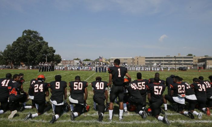Woodrow Wilson High's Edwin Lopez (#1) stands while some of his teammates kneel during the national anthem before Woodrow Wilson High School played Highland High School at Woodrow Wilson High School in Camden, N.J., Saturday, Sept. 10, 2016. Colin Kaepernick's protest against social injustices has opened discussion and debate on a national level. For high schools across the country, where a host of football players have joined the San Francisco quarterback by kneeling during the national anthem, the issue is much more personal and complicated.  (Yong Kim/The Philadelphia Inquirer via AP)