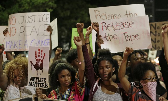 Protesters raises their fists as they march in the streets of Charlotte, N.C. Friday, Sept. 23, 2016, over Tuesday's fatal police shooting of Keith Lamont Scott. (AP Photo/Chuck Burton)