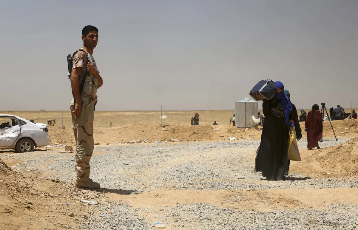A Kurdish Peshmerga soldier stands guard as displaced civilians arrive at a camp outside Irbil, 350 kilometers north of Baghdad, Iraq. (AP Photo)