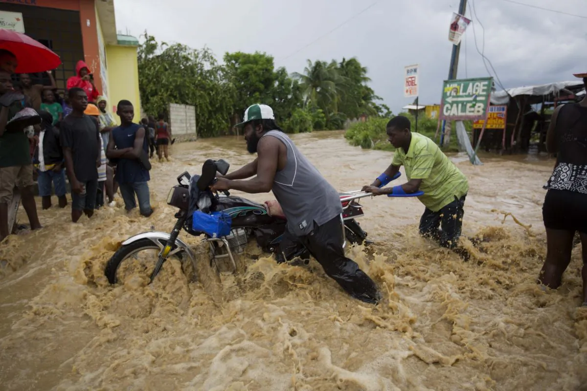 Men push a motorbike through a street flooded by a river that overflowed from heavy rains caused by Hurricane Matthew in Leogane, Haiti on Oct. 5, 2016. (AP Photo/Dieu Nalio Chery)