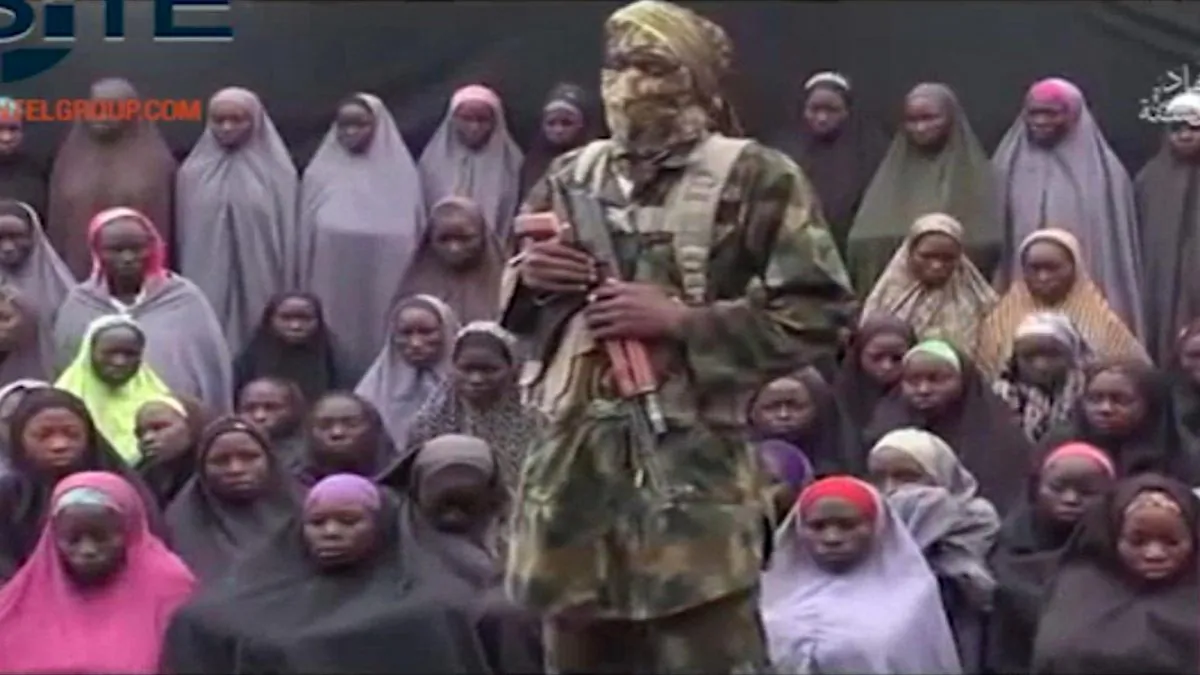 An alleged Boko Haram soldier standing in front of a group of girls alleged to be some of the 276 abducted Chibok schoolgirls held since April 2014, in an unknown location. (Militant video/Site Institute via AP)