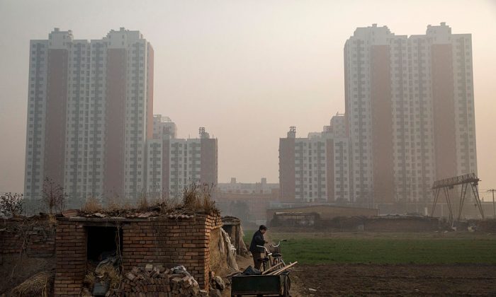 An elderly Chinese farmer stands outside her home on farmland backdropped by a new housing development outside Beijing on Nov. 21, 2014. (Kevin Frayer/Getty Images)