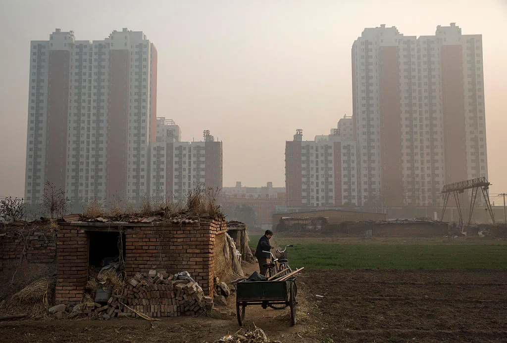 An elderly Chinese farmer stands outside her home on farmland backdropped by a new housing development outside Beijing on Nov. 21, 2014. (Kevin Frayer/Getty Images)