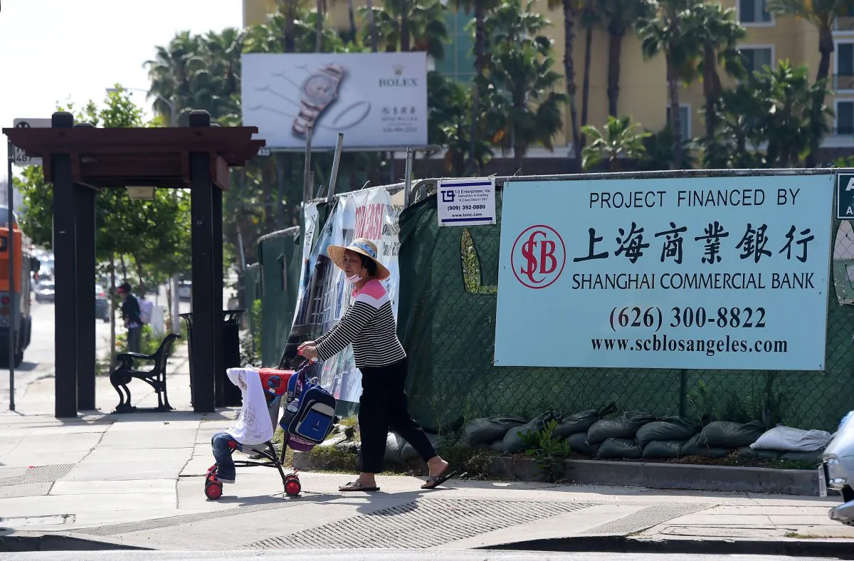 A woman pushes a stroller past a banner at a construction site project financed by the Shanghai Commercial Bank in San Gabriel, Calif., on May 17, 2016. (Frederic J. Brown /AFP/Getty Images)
