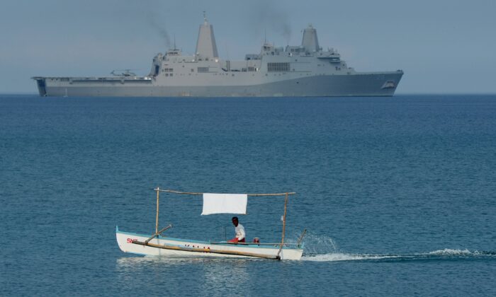 Filipiński rybak jest widziany obok amfibijnego statku transportowego US Navy USS Green Bay (LPD-20) podczas ćwiczeń desantowych na plaży w San Antonio w prowincji Zambales w dniu 21 kwietnia 2015 r., W ramach corocznych wspólnych manewrów filipińsko-amerykańskich około 220 kilometrów (137 mil) na wschód od Scarborough Shoal na Morzu Południowochińskim. Filipiny wyraziły 20 kwietnia alarm o chińskiej "agresywności" na spornych wodach regionalnych, gdy rozpoczęły gigantyczne gry wojenne ze Stanami Zjednoczonymi, które częściowo miały na celu strzał ostrzegawczy dla Pekinu. AFP PHOTO/TED ALJIBE (Zdjęcie powinno brzmieć TED ALJIBE/AFP/Getty Images)