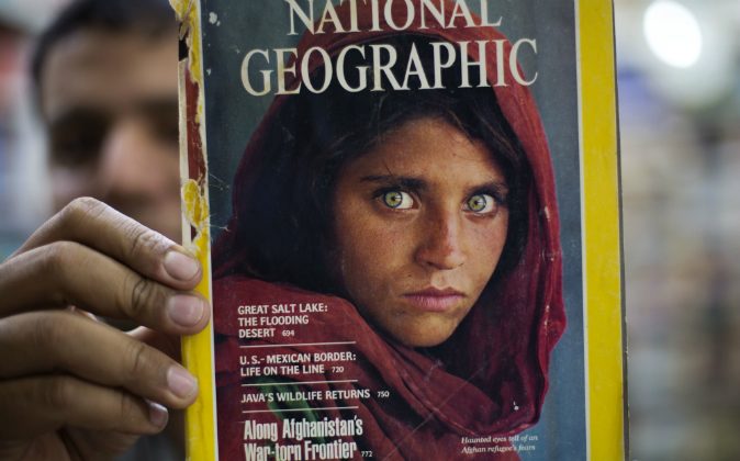 Pakistan's Inam Khan, owner of a book shop shows a copy of a magazine with the photograph of Afghan refugee woman Sharbat Gulla, from his rare collection in Islamabad, Pakistan, Wednesday, Oct. 26, 2016. A Pakistani investigator says the police have arrested National Geographic's famed green-eyed 'Afghan Girl' for having a fake Pakistani identity card. Shahid Ilyas from the Federal Investigation Agency, says the police arrested Sharbat Gulla during a raid on Wednesday at a home in Peshawar. (AP Photo/B.K. Bangash)


