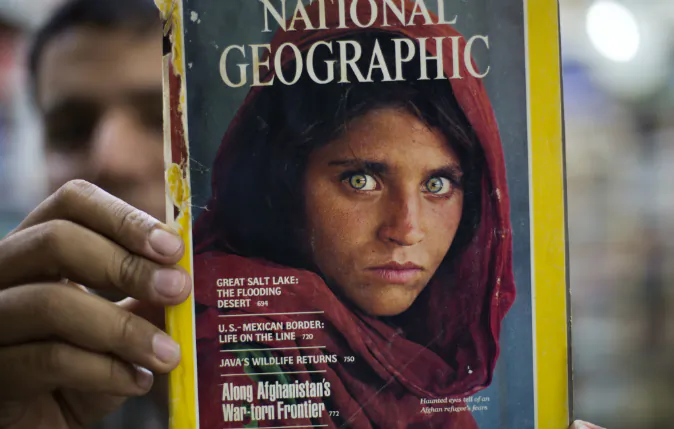 Pakistan's Inam Khan, owner of a book shop shows a copy of a magazine with the photograph of Afghan refugee woman Sharbat Gulla, from his rare collection in Islamabad, Pakistan, Wednesday, Oct. 26, 2016. A Pakistani investigator says the police have arrested National Geographic's famed green-eyed 'Afghan Girl' for having a fake Pakistani identity card. Shahid Ilyas from the Federal Investigation Agency, says the police arrested Sharbat Gulla during a raid on Wednesday at a home in Peshawar. (AP Photo/B.K. Bangash)