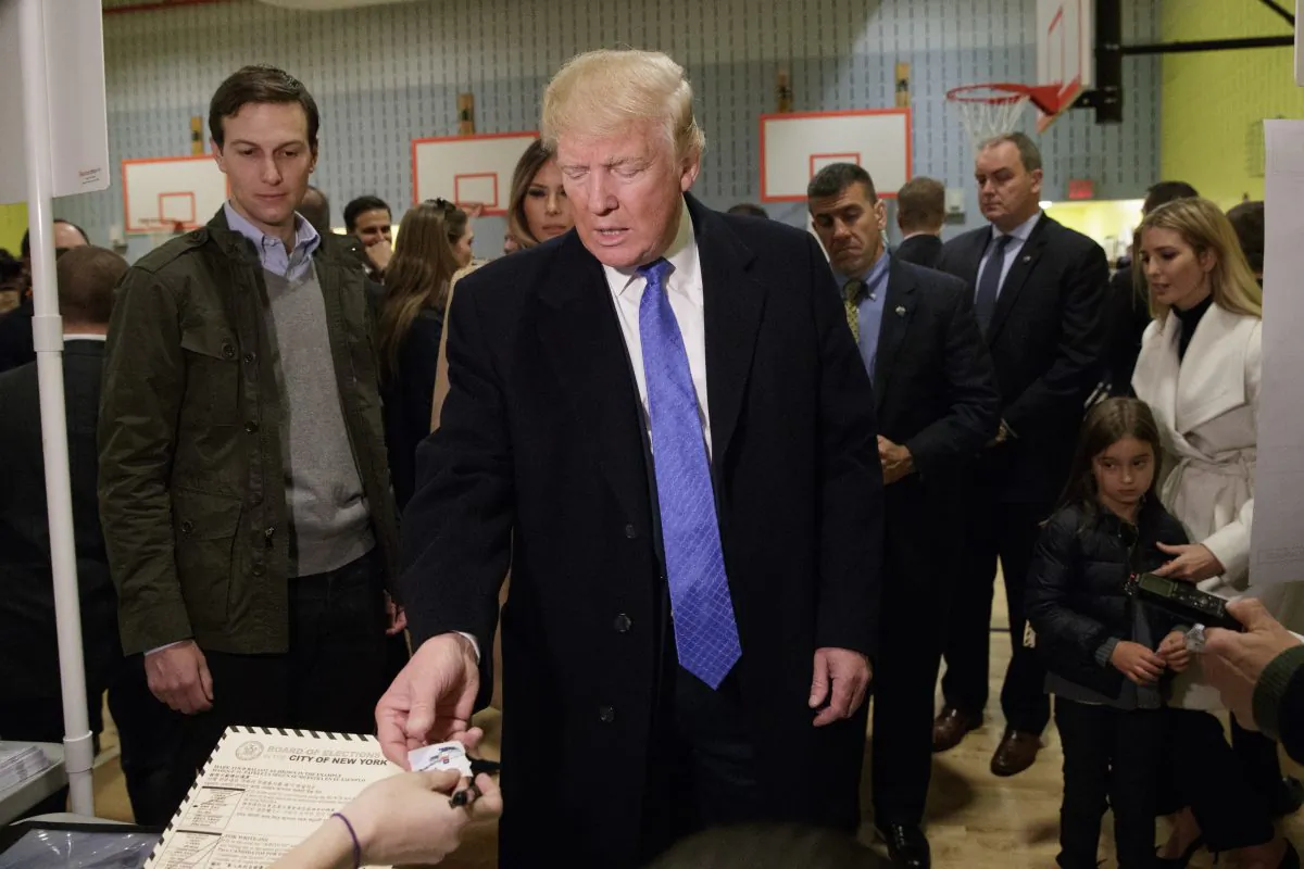 Republican presidential candidate Donald Trump is handed a sticker before casting his ballot at PS-59,  in New York on Nov. 8, 2016. (AP Photo/ Evan Vucci)