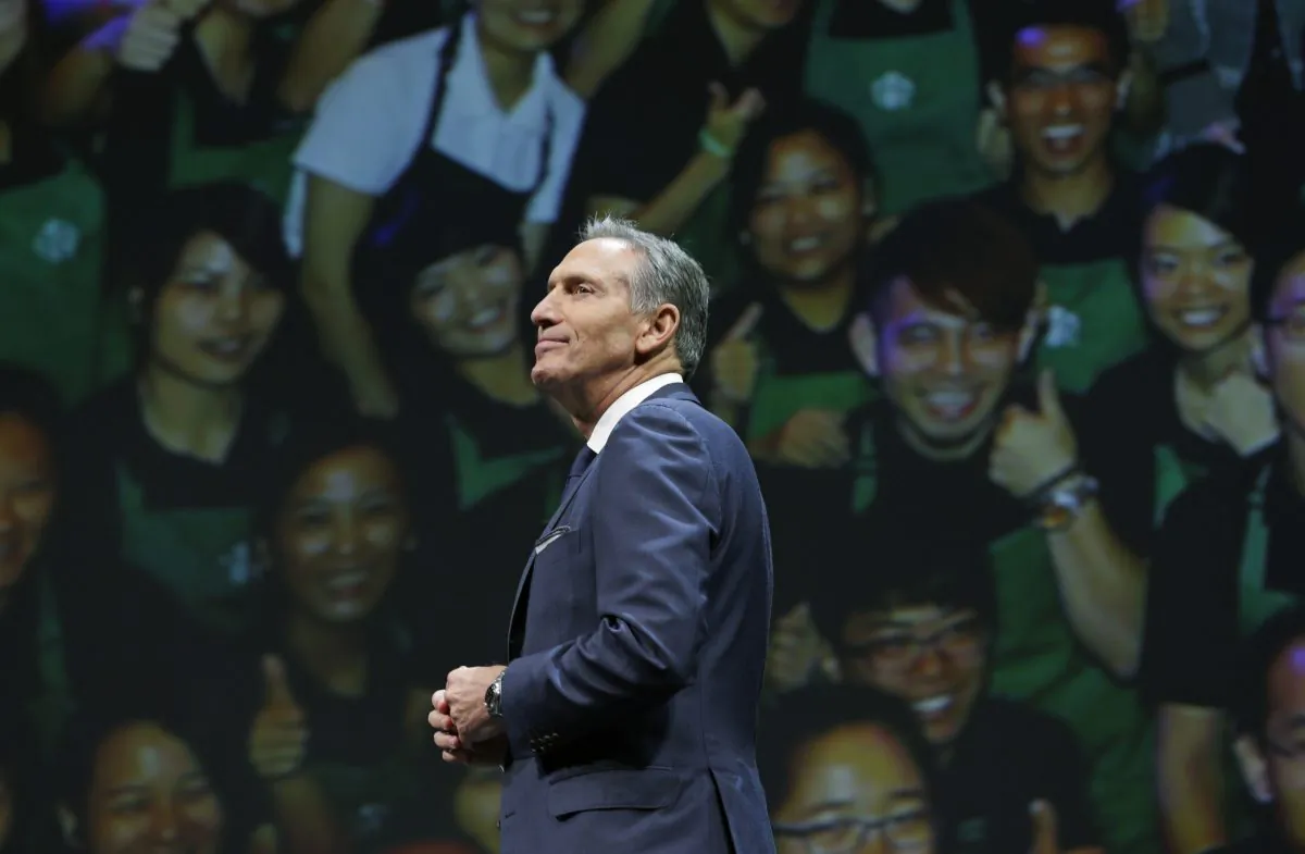 Starbucks CEO Howard Schultz walks in front of a photo of Starbucks baristas, at the coffee company's annual shareholders meeting in Seattle, in this file photo.
 (Ted S. Warren/AP Photo)