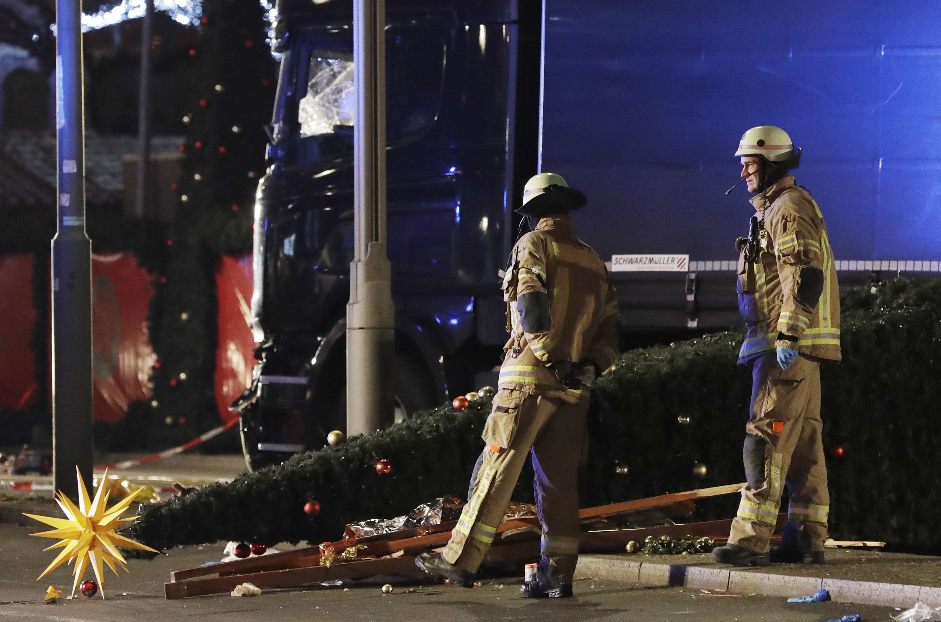 Firefighters look at a toppled Christmas tree after a truck ran into a crowded Christmas market and killed several people in Berlin, Germany on Dec. 19, 2016. (AP Photo/Michael Sohn)
