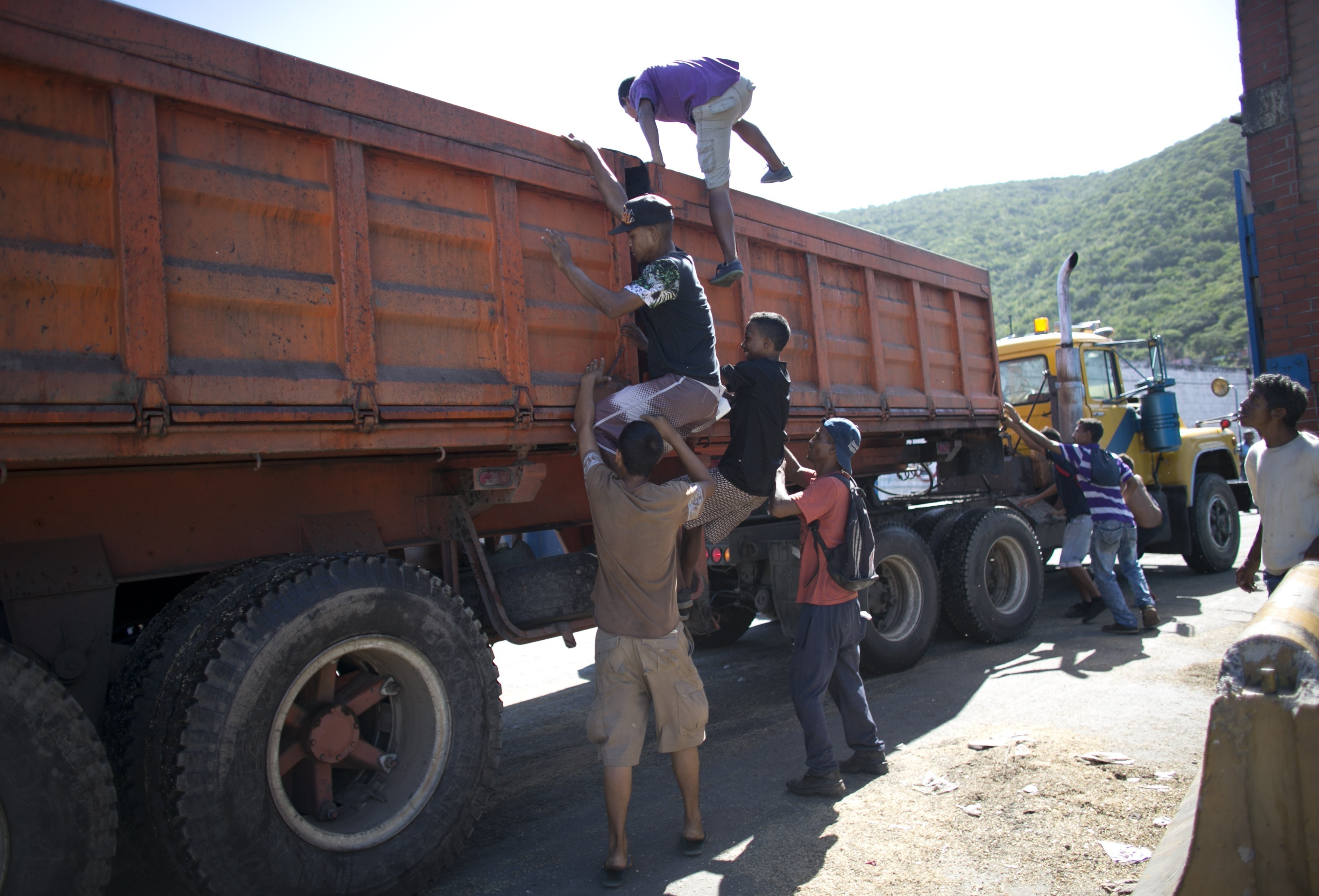 Young men climb into an empty food truck, in search of leftover grain, as the vehicle comes to a slow stop outside the port in Puerto Cabello, Venezuela on Nov. 14, 2016. (AP Photo/Ariana Cubillos)