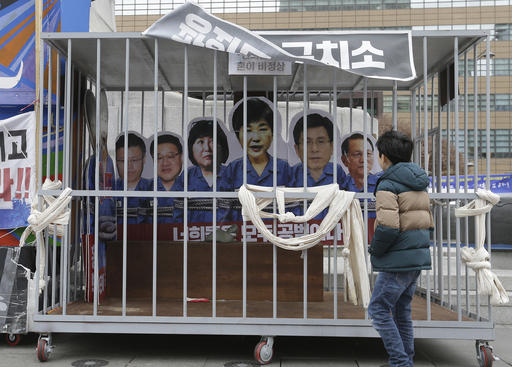 A boy looks at portraits of impeached South Korea's President Park Geun-hye, center, and her aides in a mock jail cell in Seoul, South Korea, on Jan. 5, 2017. (AP Photo/Ahn Young-joon)