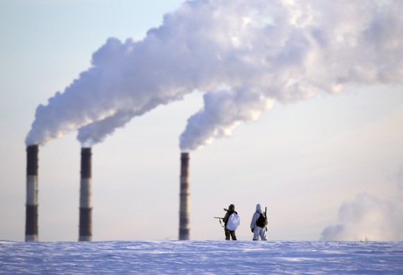 People hunting small animals cross the terrain as smoke is released from a heating plant in morning temperatures of -19 degrees Celsius (-2.2 degrees Fahrenheit) in Minsk, Belarus, Monday, Jan. 9, 2017. (AP Photo/Sergei Grits)