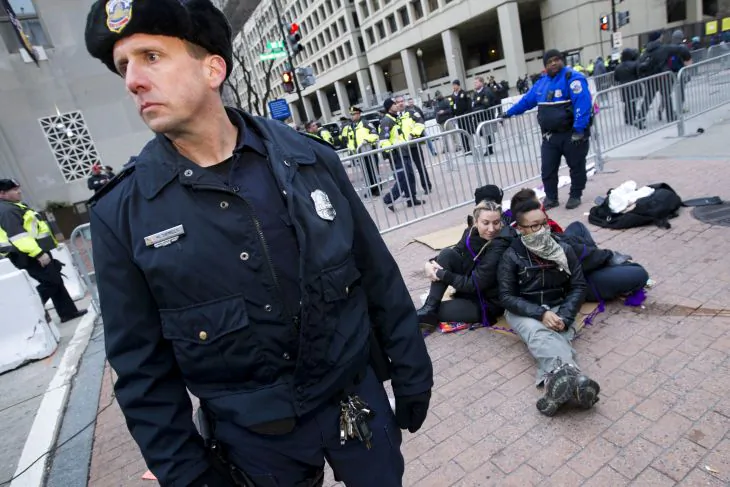 Demonstrators sit near a security checkpoint as police officers let people pass to the inauguration, Friday, Jan. 20, 2017 in Washington, ahead of President-elect Donald Trump's inauguration. ( AP Photo/Jose Luis Magana)