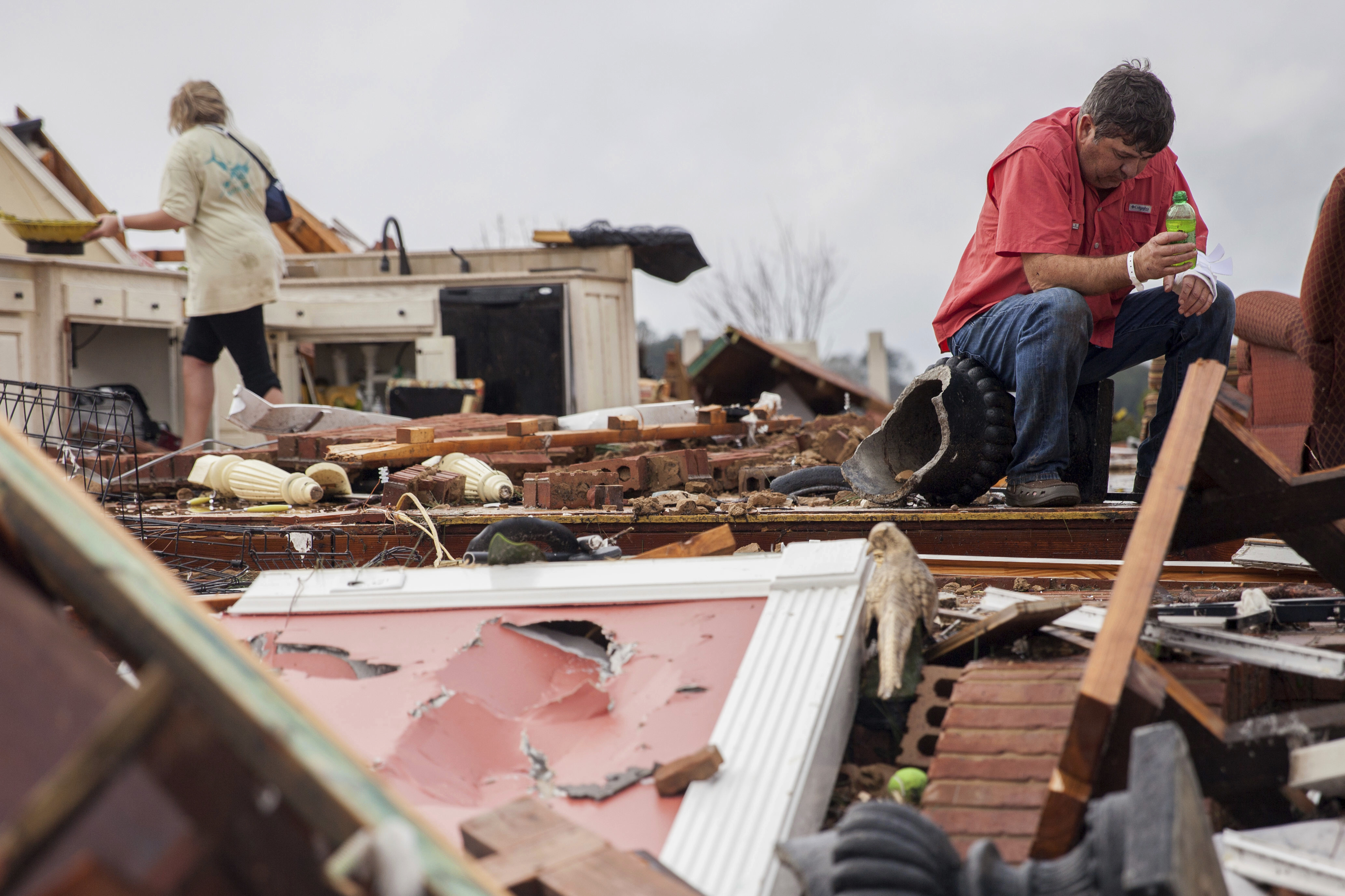 Jeff Bullard sits in what used to be the foyer of his home as his daughter, Jenny Bullard, looks through debris at their home that was damaged by a tornado in Ga., on Jan. 22, 2017, in Adel. (AP Photo/Branden Camp)