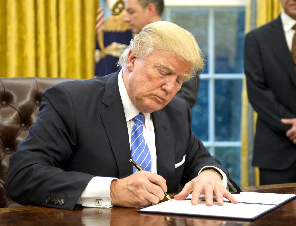President Donald Trump signs the last of three Executive Orders in the Oval Office of the White House in Washington, on Jan. 23, 2017. (Ron Sachs - Pool/Getty Images)