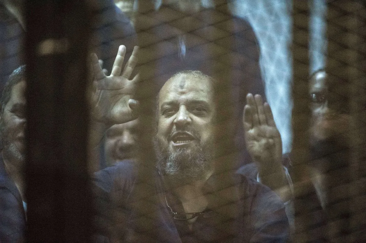 Egyptian Muslim Brotherhood top figure Mohamed al-Beltagy flashes the four-finger symbol known as "Rabaa" from behind the defendant's cage as the judge reads out the verdict sentencing him and more than 100 other defendants, at the police academy in Cairo on May 16, 2015. (Khaled Desouki /AFP/Getty Images)