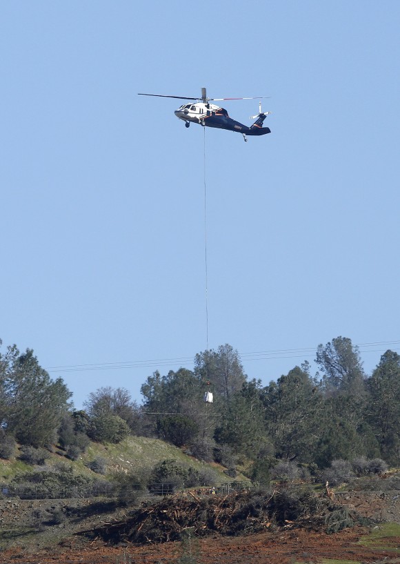 A helicopter lowers a load of rocks to fill in a hole near the Oroville Dam's emergency spillway, Tuesday, Feb. 14, 2017, in Oroville, Calif. The barrier, at the nation's tallest dam, is being repaired after authorities ordered mass evacuations for everyone living below the lake out of concerns the spillway could fail and send a 30-foot wall of water roaring downstream. (AP Photo/Rich Pedroncelli)