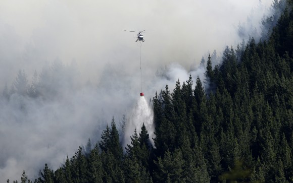 A helicopter dumps water on a wild fire in the Port Hills near Christchurch, New Zealand, Tuesday, Feb. 14, 2017. Up to 15 helicopters, and over 100 firefighters have been battling two massive wildfires that have burnt over 700 hectares since erupting on Monday evening. (AP Photo/Mark Baker)