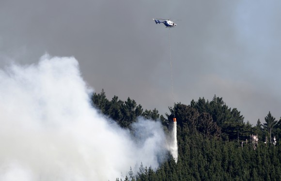 A helicopter dumps water on a wild fire in the Port Hills near Christchurch, New Zealand, Tuesday, Feb. 14, 2017. Up to 15 helicopters, and over a 100 firefighters have been battling two massive wildfires that have burnt over 700 hectares since erupting on Monday evening. (AP Photo/Mark Baker)