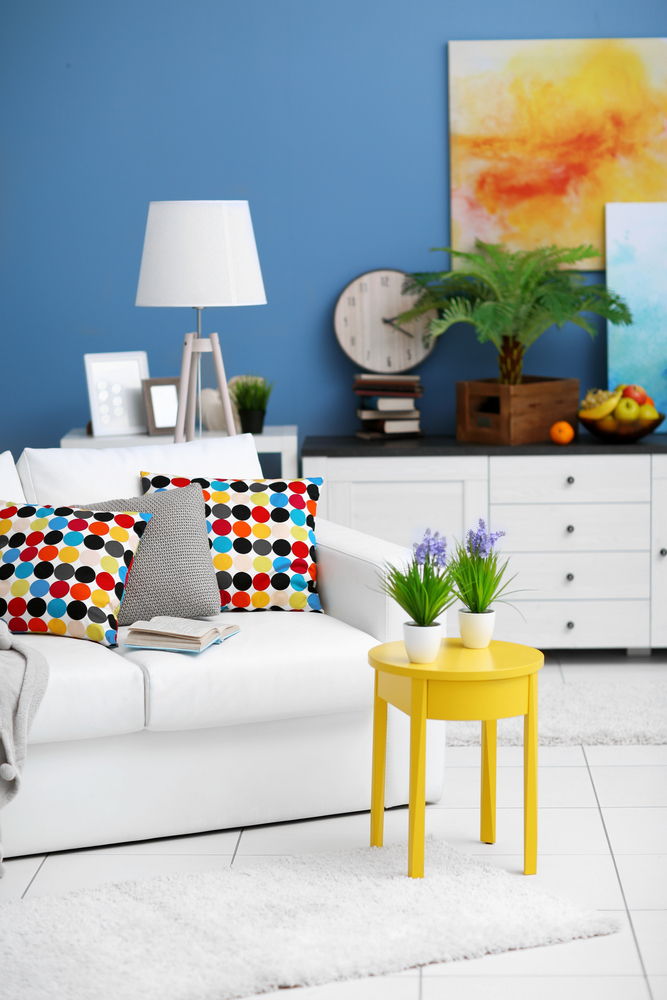A rich blue feature wall makes a striking backdrop for a soft white sofa and a mix of colourful accessories. (Africa studio/Shutterstock)