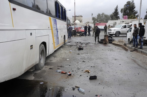 In this photo released by the Syrian official news agency SANA, people inspect damage in a parking lot at the site of an attack by twin explosions in Damascus, Syria, Saturday, March 11, 2017. Twin explosions Saturday near religious shrines frequented by Shiite pilgrims in the Syrian capital Damascus killed dozens of people, Arab media and activists report. (SANA via AP)