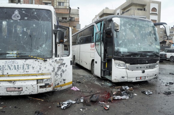 In this photo released by the Syrian official news agency SANA shows blood soaked streets and several damaged buses in a parking lot at the site of an attack by twin explosions in Damascus, Syria, Saturday, March 11, 2017. Twin explosions Saturday near religious shrines frequented by Shiite pilgrims in the Syrian capital Damascus killed dozens of people, Arab media and activists report. (SANA via AP)