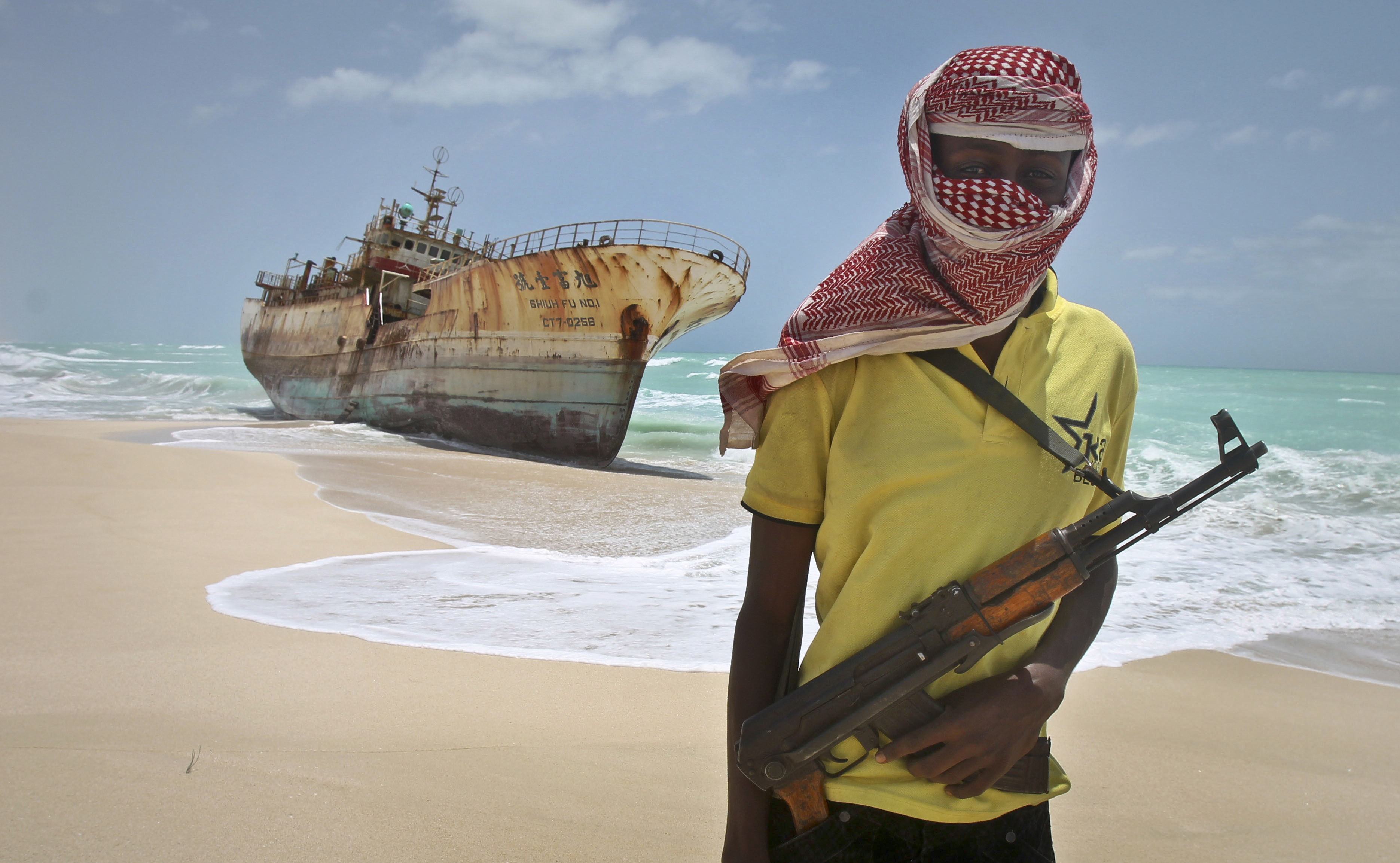 Masked and armed Somali pirate Hassan stands near a Taiwanese fishing vessel washed ashore after the pirates were paid a ransom and the crew were released in the once-bustling pirate den of Hobyo, Somalia on Sept. 23, 2012. (AP Photo/Farah Abdi Warsameh)