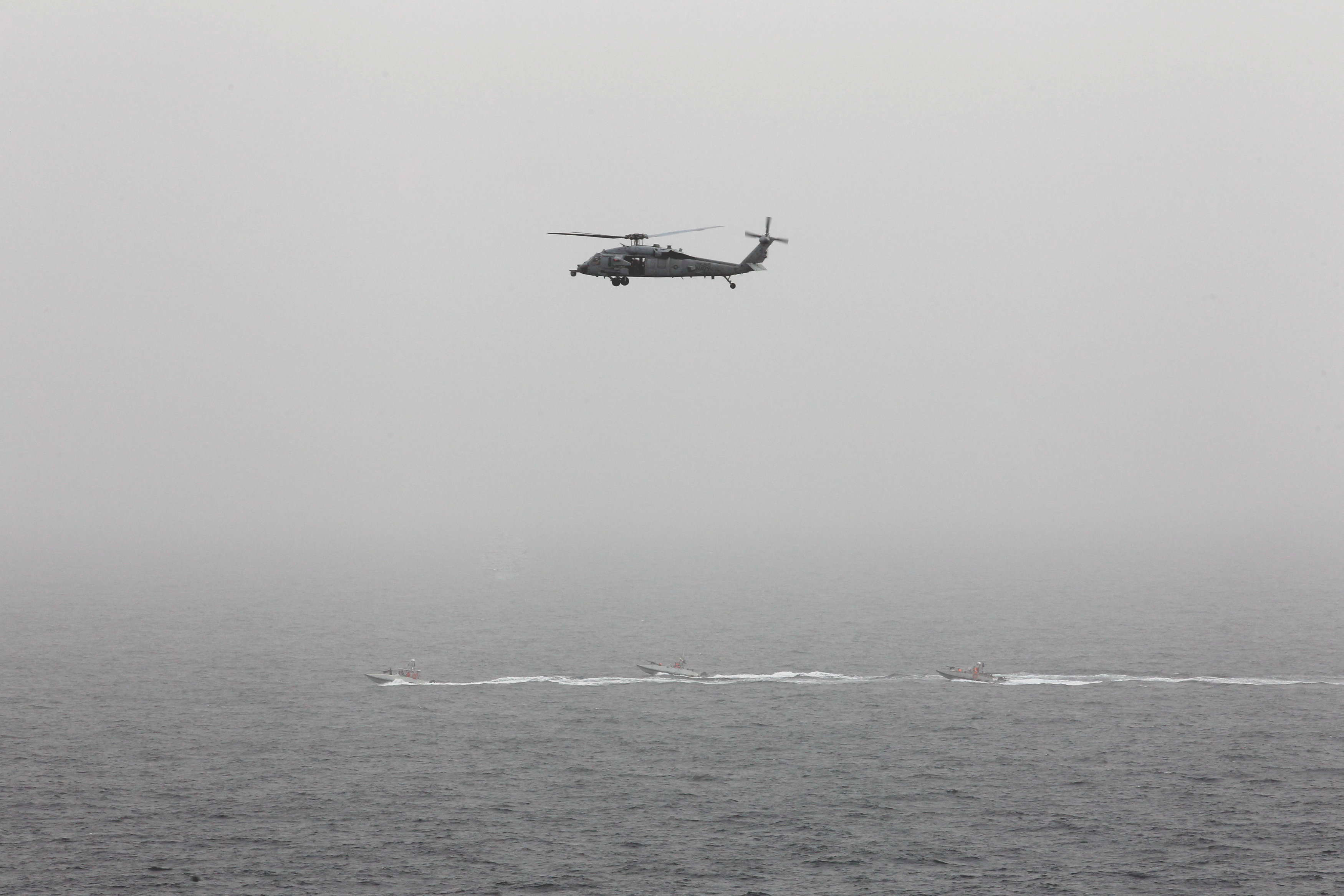 Three Iranian Revolutionary Guard boats are seen near the U.S. aircraft carrier, USS George H. W. Bush while transiting Straits of Hormuz as U.S. Navy helicopter hovers over them during early hours of March 21, 2017. (REUTERS/Hamad I Mohammed)