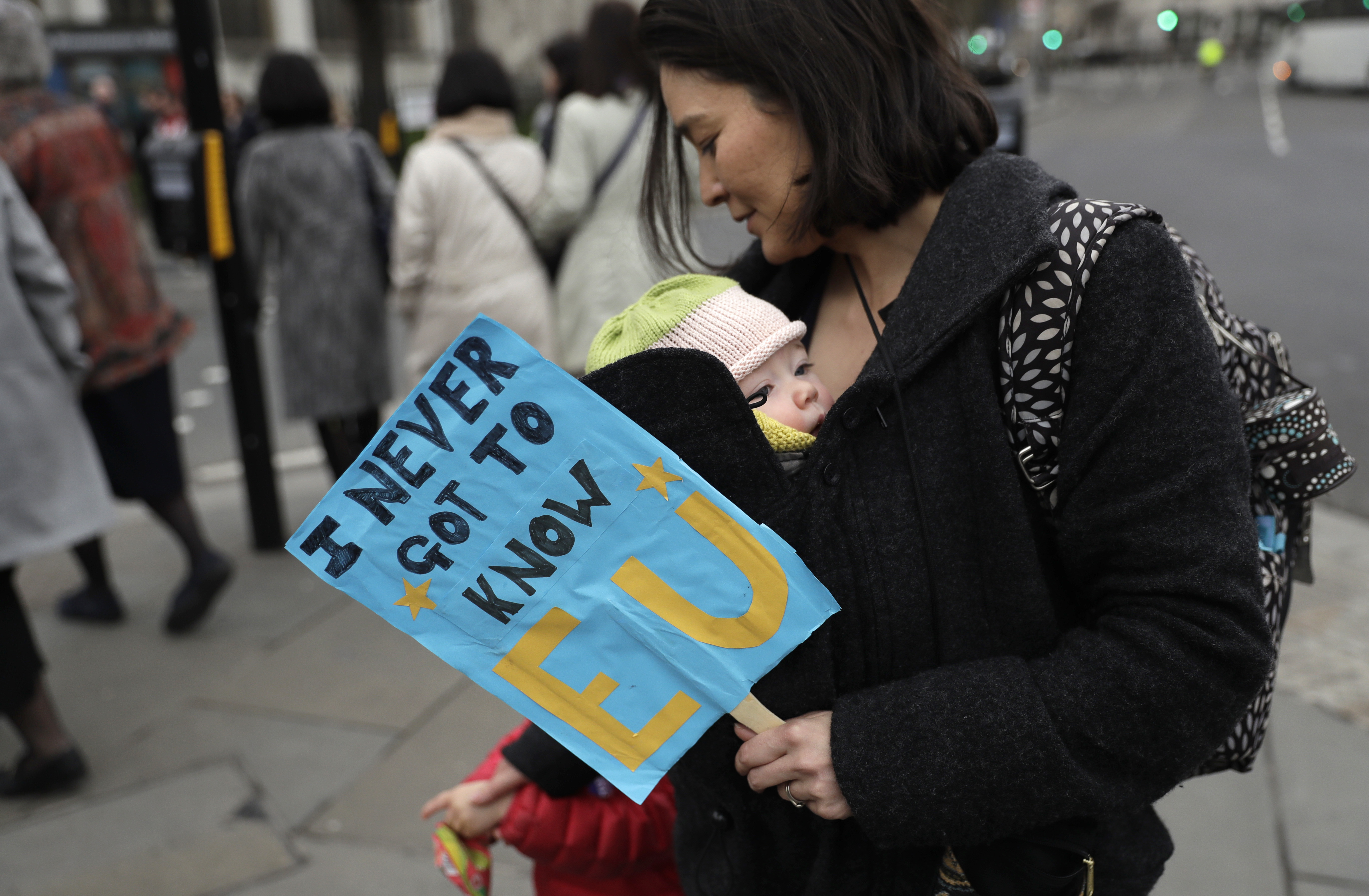 A woman carries a baby and holds a banner as she takes part in a protest outside the House of Commons in central London on March 29, 2017. (AP Photo/Matt Dunham)