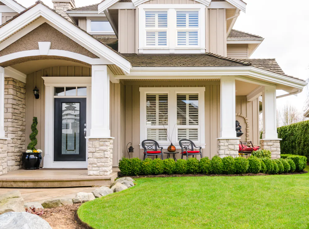 A trimmed boxwood hedge, rattan chairs, and a black ceramic pot matching the front door gives this home a clean and tailored look. (ppa/Shutterstock)